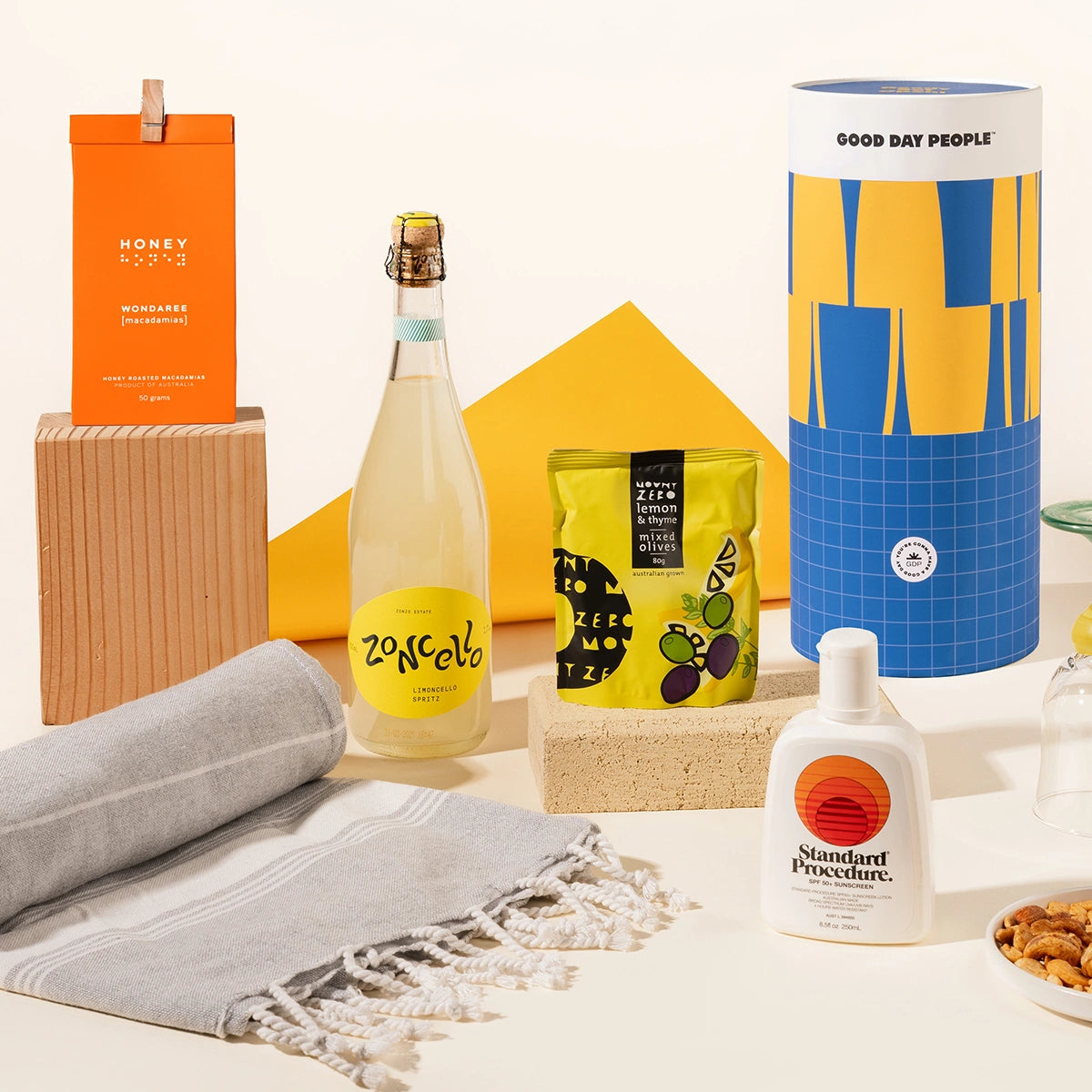 Summer-inspired gift hamper with Zoncello limoncello spritz, Standard procedure sunscreen, olives, a turkish beach towel and nuts, packaged in a fun canister.