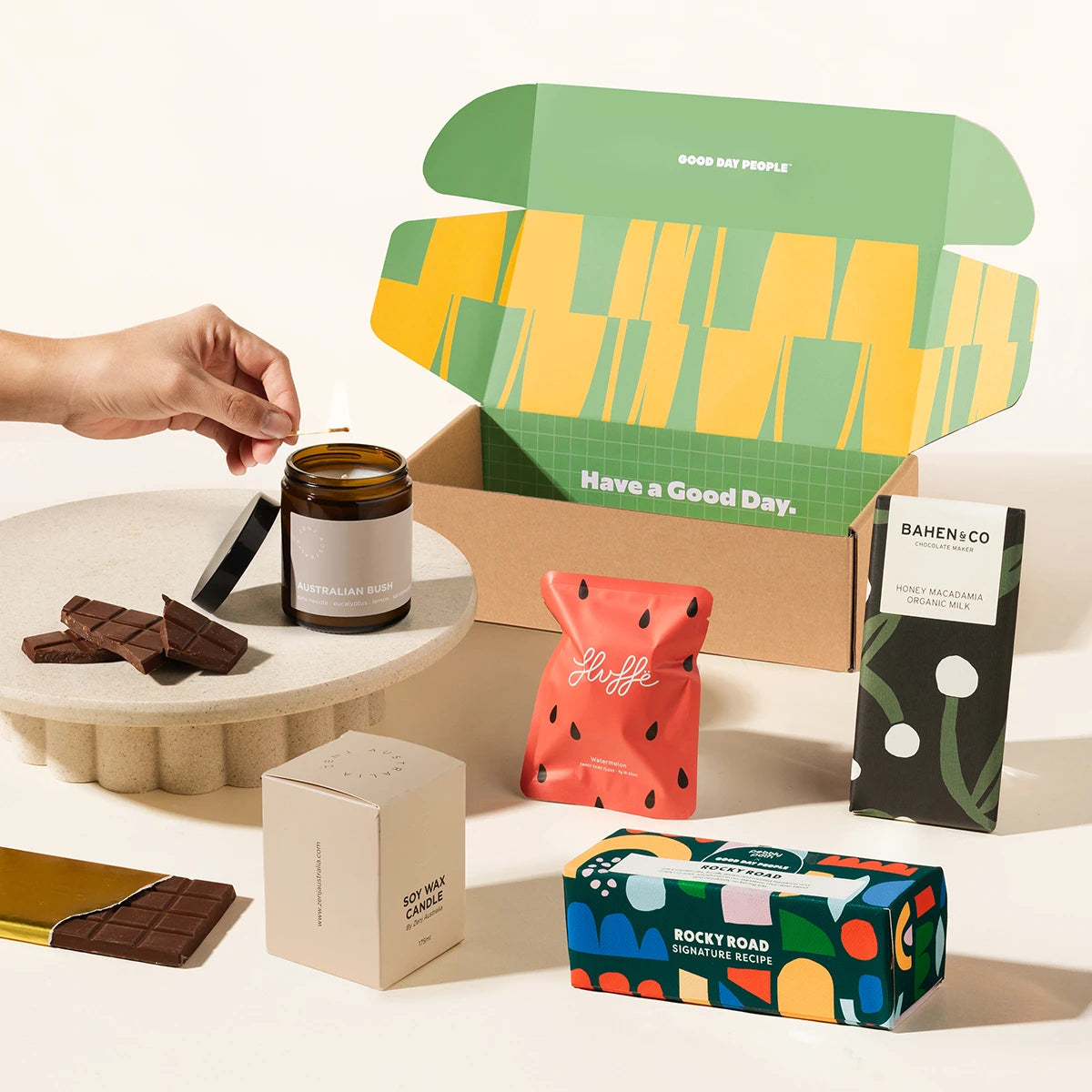 A curated gift box set on a clean white background featuring a soy candle, fairy floss, rocky road and organic chocolate bar. A graphic gift box with "have a Good Day." on it.