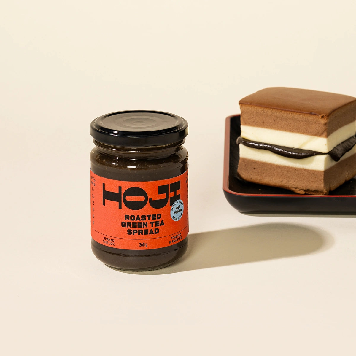 Jar of Hoji roasted green tea or hojicha spread next to a layered dessert on a beige background