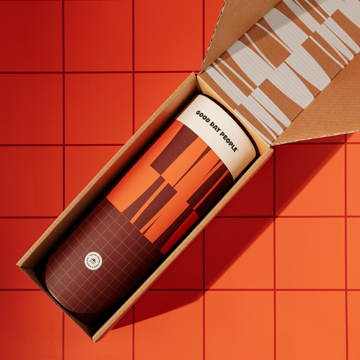 Design-forward gift canister in burgundy and orange, contained in a branded shipping carton