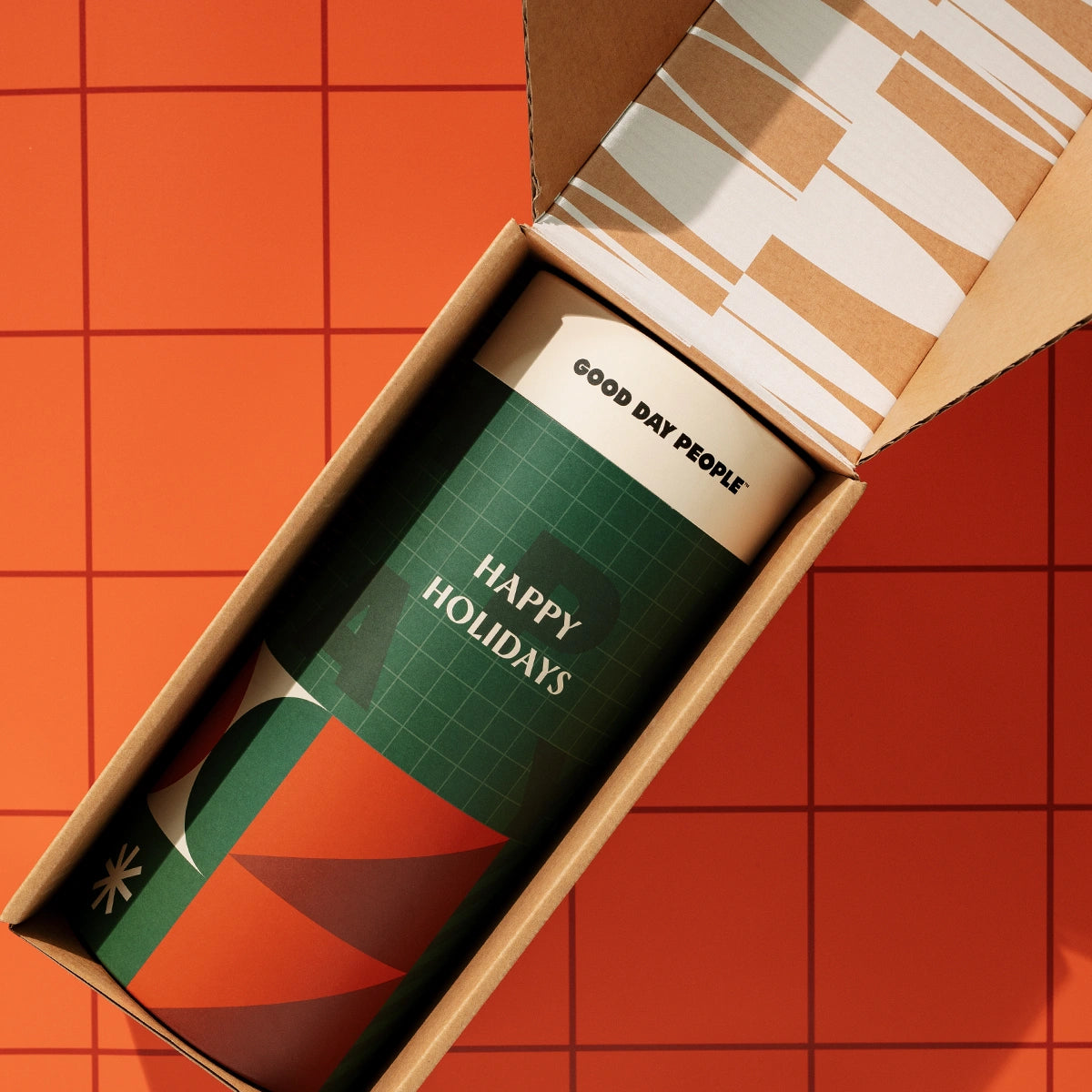 Christmas packaging canister with "Happy Holidays" on it. Geometric green and red design. Fun, vibrant and trendy packaging. Canister in a branded shipping carton.