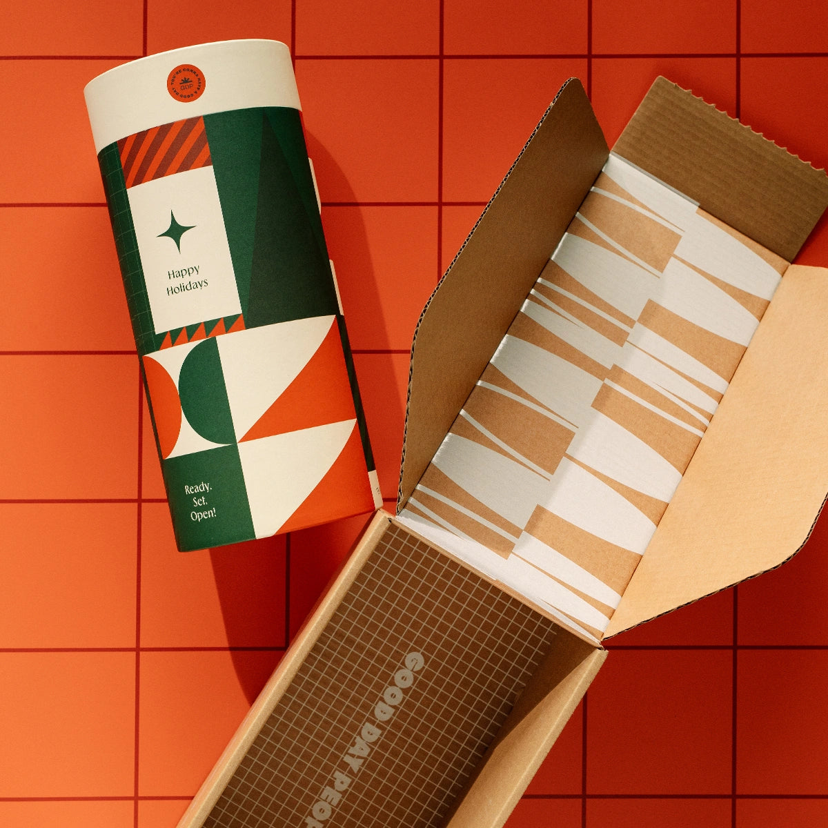 Christmas packaging canister with "Happy Holidays" on it. Geometric green and red design. Fun, vibrant and trendy packaging. Canister in a branded shipping carton.