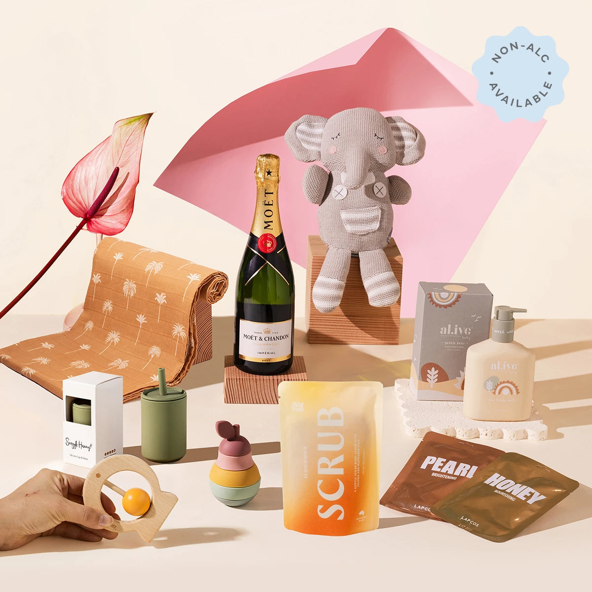 A styled gift set featuring a Moët & Chandon, an elephant plush toy, a scrub pouch, swaddle, sippy cup, teether, toy, face masks and baby body wash.