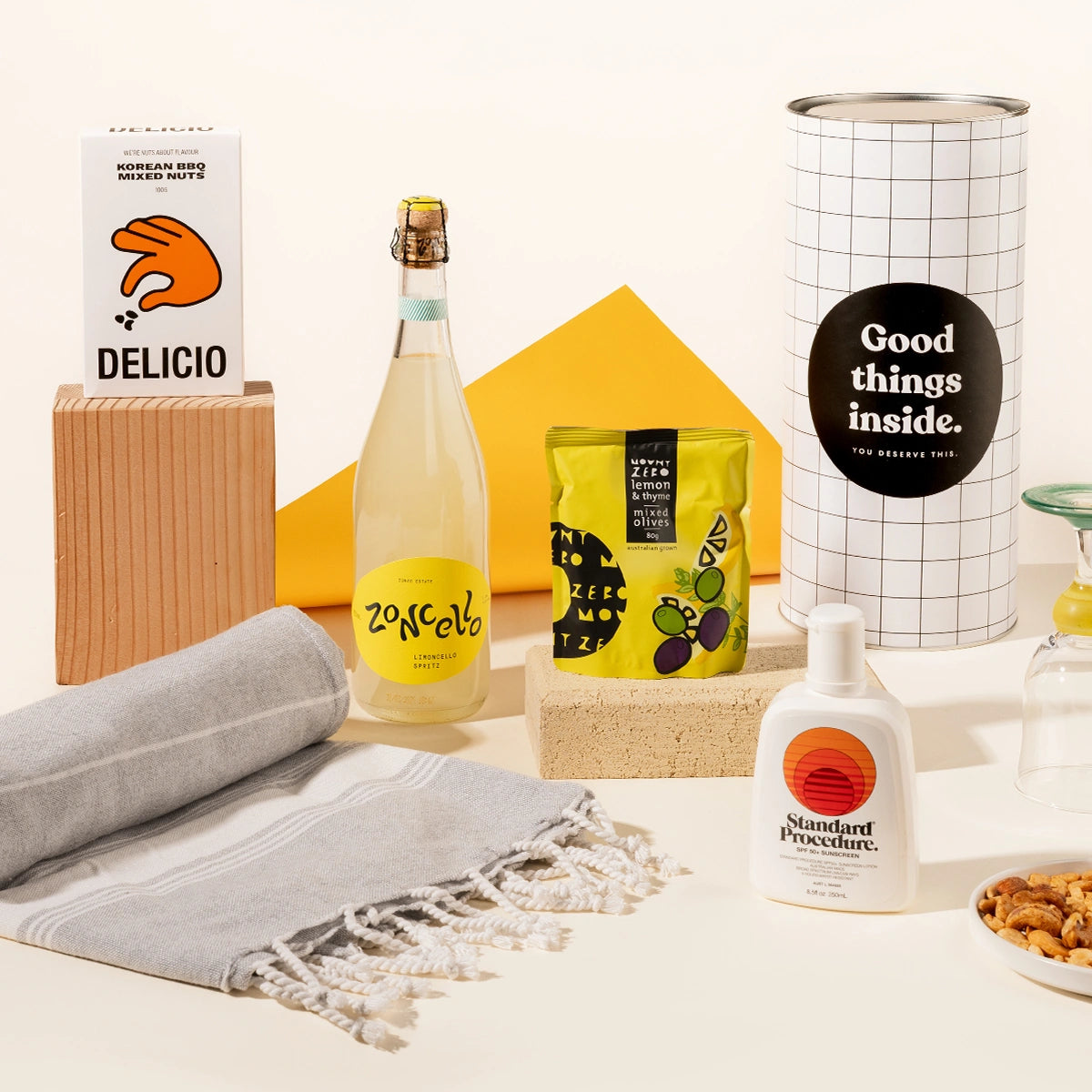 Summer-inspired gift hamper with Zoncello limoncello spritz, Standard procedure sunscreen, olives, a turkish beach towel and Korean BBQ mixed nuts, packaged in a fun canister.