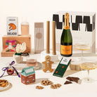 Assorted holiday gift hamper including a bottle of champagne, delicio korean bbq nuts, pillar candles, ferm living carafe and glass set, 2 champagne coupes, chocolate, gingerbread man, salted caramel pretzels and a gin bauble. All packaged in a beautiful gift box. 