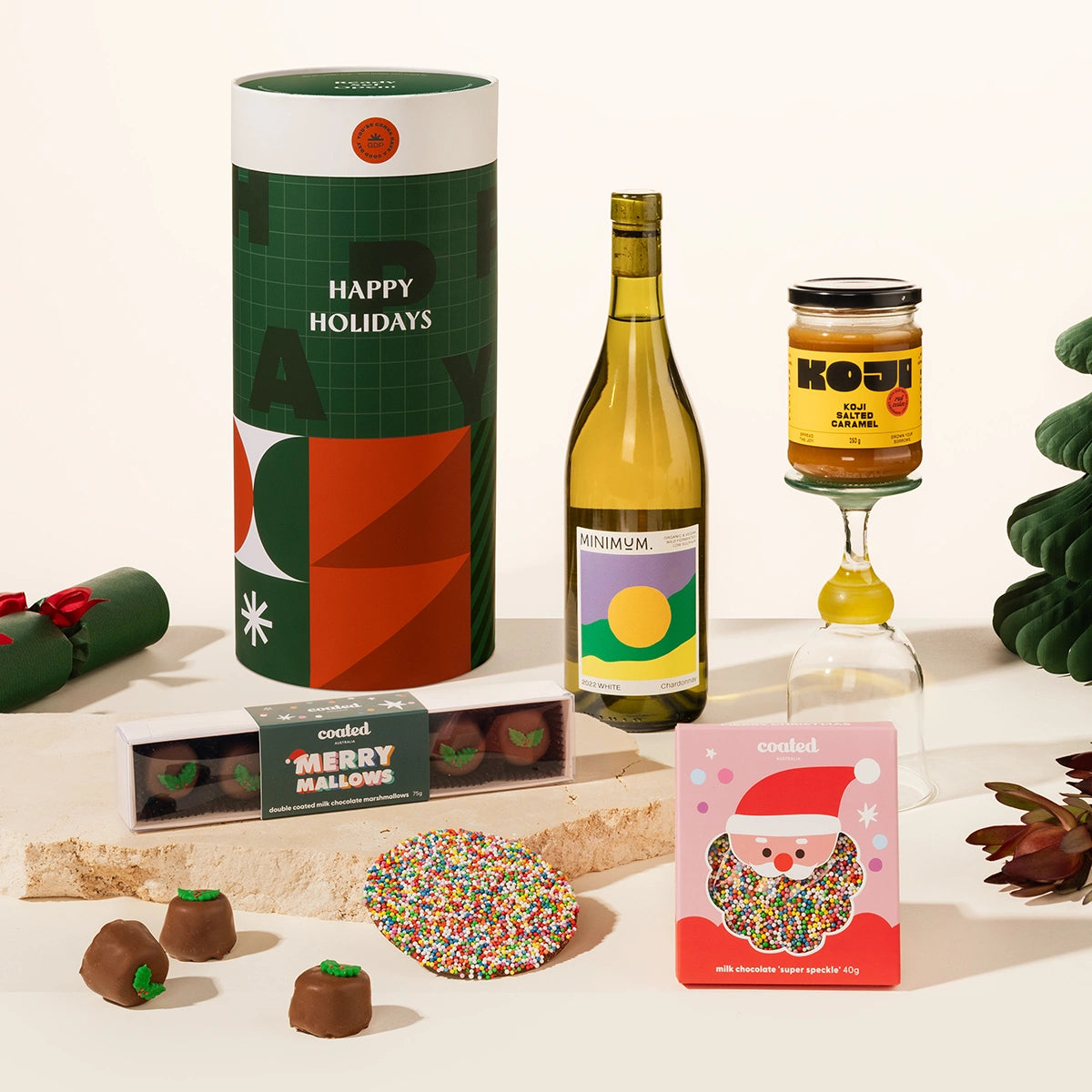Christmas gift hamper including a bottle of wine, a jar of miso caramel, and a box of chocolate coated marshmallows and a speckled milk chocolate. 