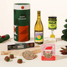 Christmas gift hamper including a bottle of wine, a jar of matcha spread, and a box of chocolate coated marshmallows and a speckled milk chocolate. 