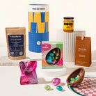 The Dashing Darcy Gift Hamper including a pack of chocolate powder, a jar of Koji, a box of chocolate Easter eggs, and a bag of roasted nuts on a white background.