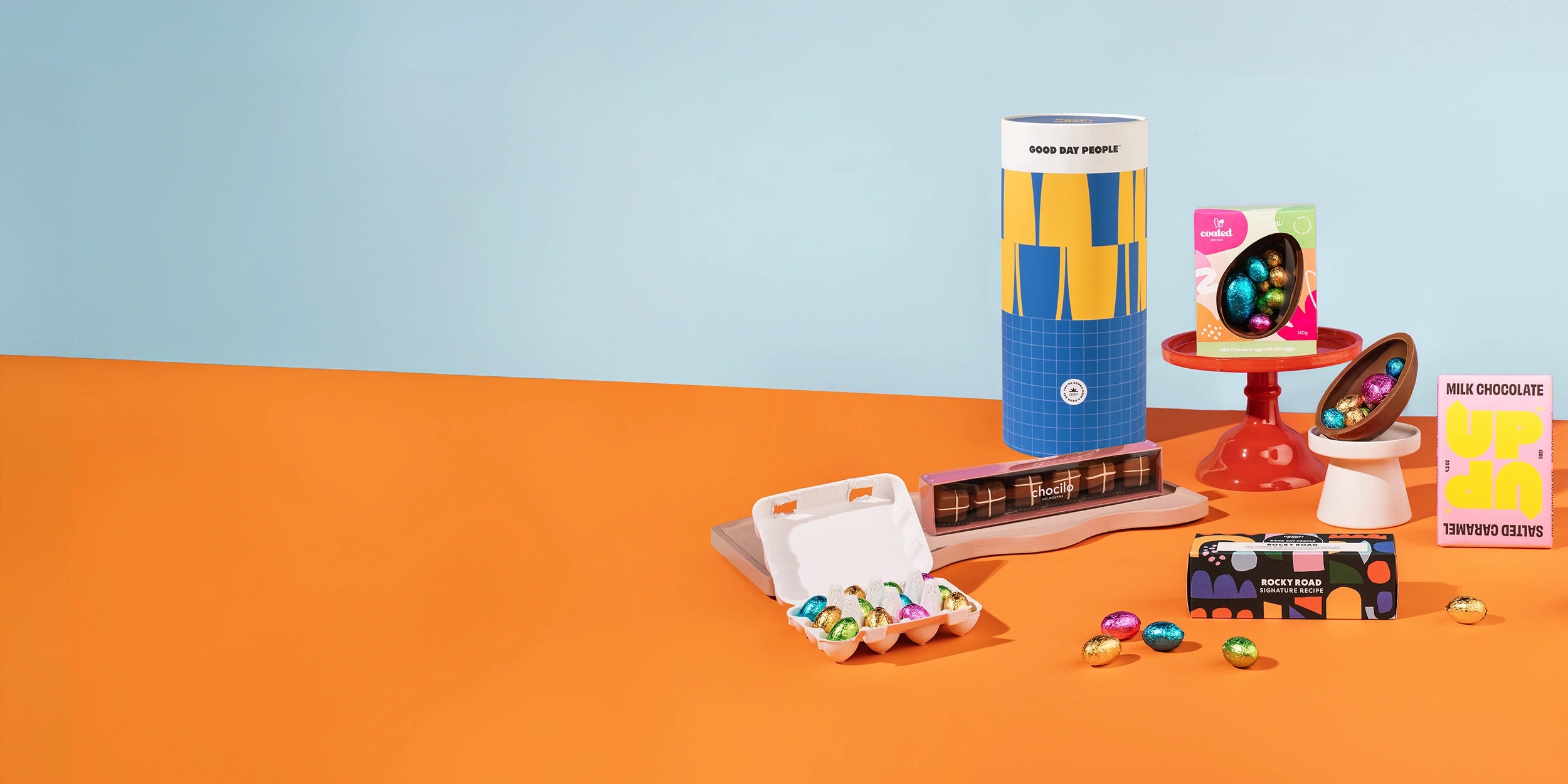 Colorful stationery items including an egg-shaped container, a box of crayons, and a small stand with colorful objects on a blue and orange background.