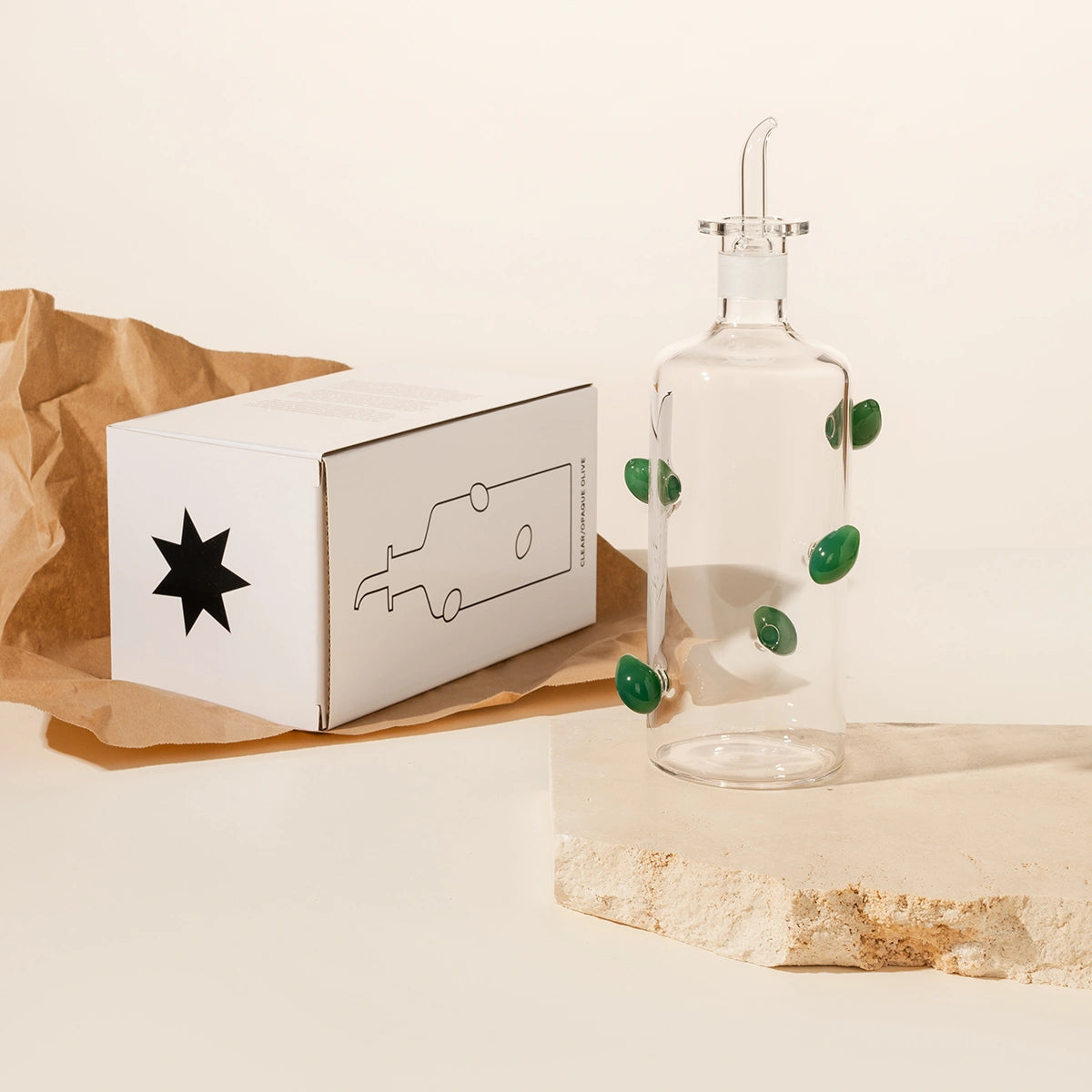 Glass bottle with green olive accents and a white box on a beige background
