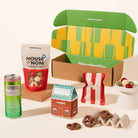 A curated gift box set featuring a green and yellow patterned box from Good Day People, a bag of House of Nom chocolate nuts, a can of St. Ali Strawberry iced matcha, chocolate pretzels and fairy floss.