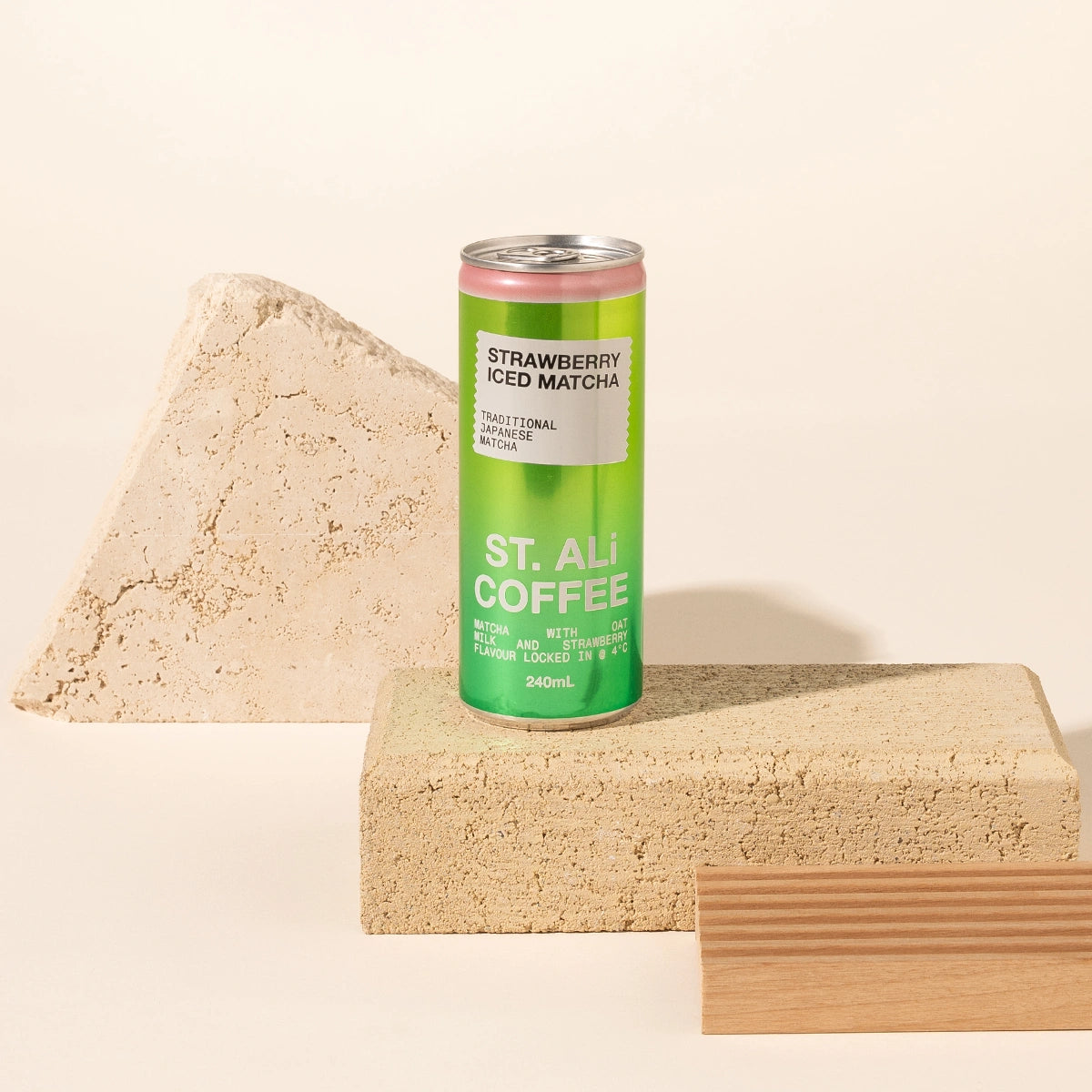 A 240ml can of St. Ali Strawberry Iced Matcha stands on a textured beige block, styled with a concrete pyramid and a wooden slat against a warm cream background.