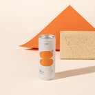 Strangelove mandarin soda can with orange graphics stands on a beige surface in front of an orange geometric backdrop and a textured beige block.