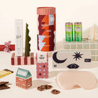 Twinkling Tina Christmas gift box styled with two St Ali Strawberry Iced Matcha cans, a Black Blaze Seaweed Candle, a pink Slowdown Studio silk eye mask, Jingle Bell Choc and chocolate coated pretzels, next to a red and white striped Christmas canister